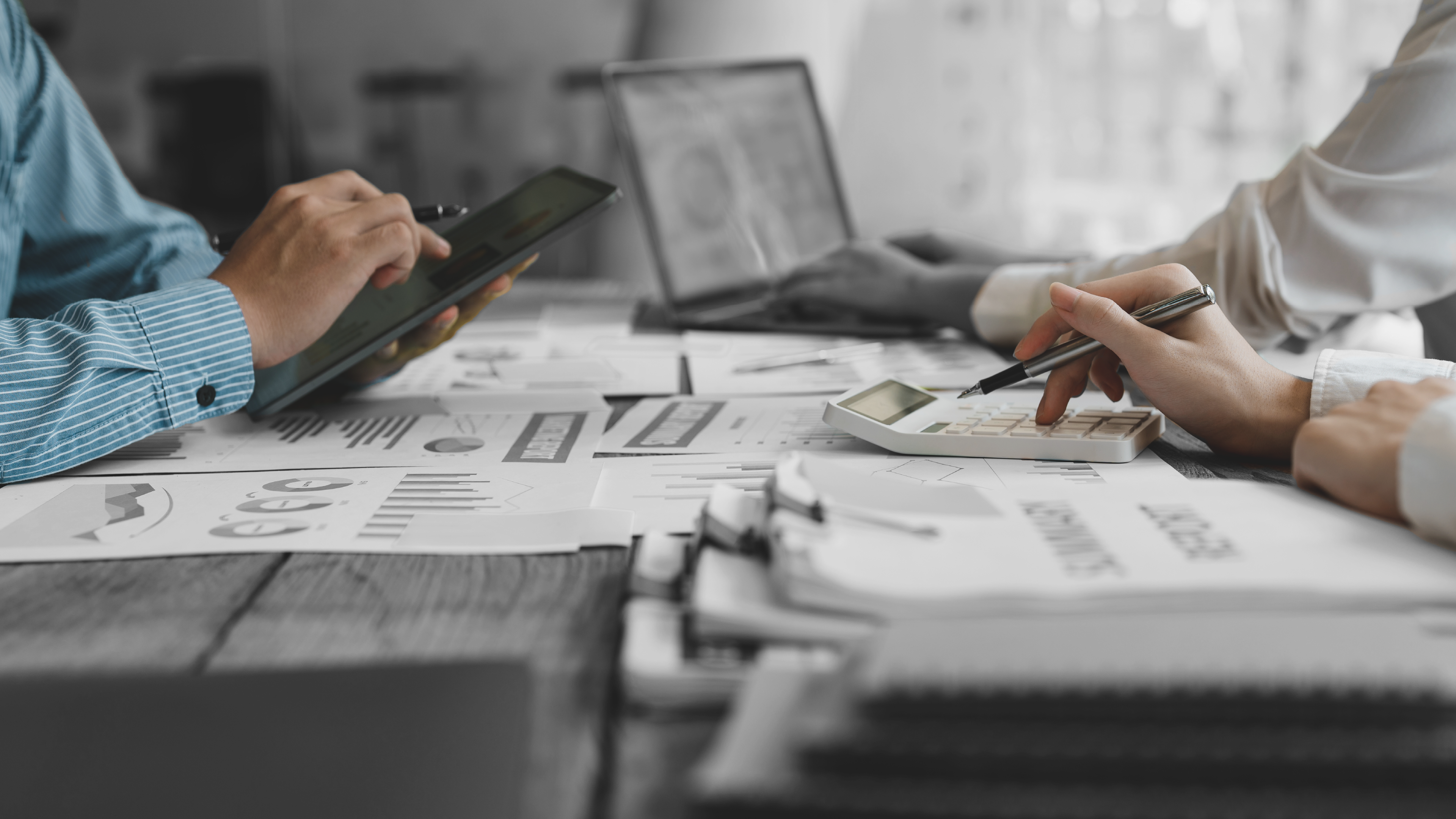 Imagen de personas trabajando con computadora, tableta y escribiendo a mano en una mesa