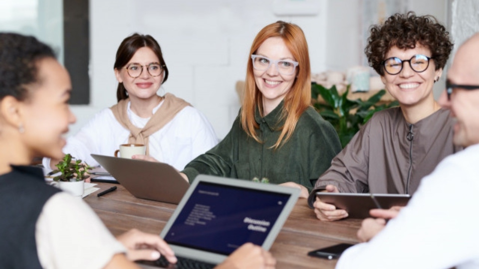 Imagen de un grupo de personas sonriendo y trabajando juntas en una mesa con portátiles y tabletas